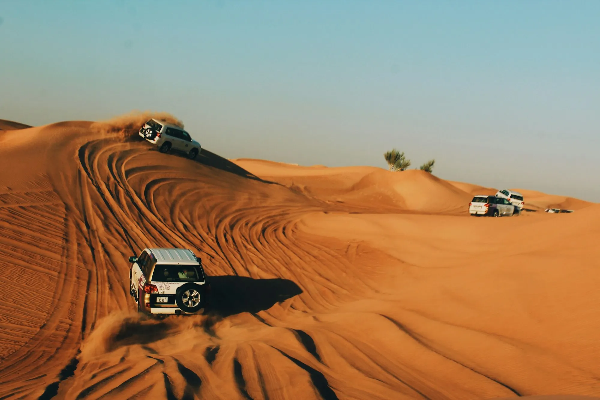 White 4x4 vehicles dune bashing across orange sand dunes in the Dubai desert