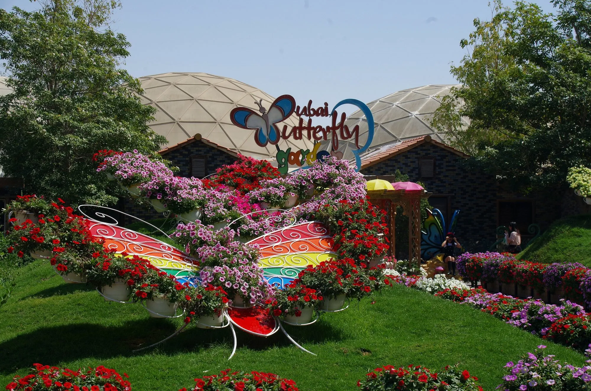 Entrance to Dubai Butterfly Garden with a giant floral rainbow butterfly and the garden domes behind