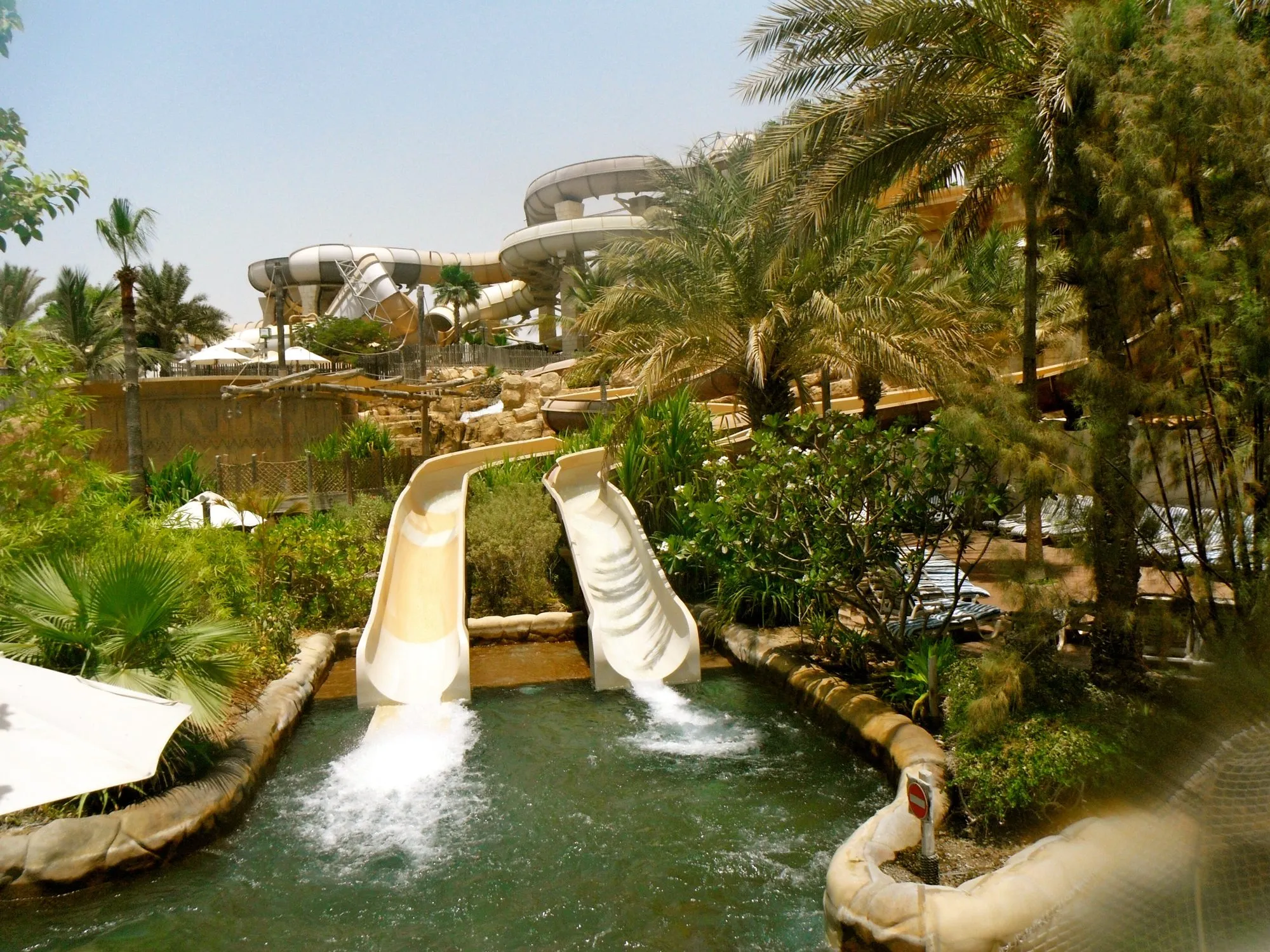Twin water slides dropping into a splash pool among palm trees at Wild Wadi Waterpark, Jumeirah, Dubai